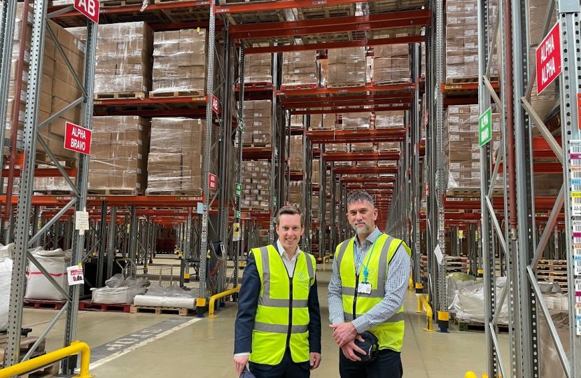 Tom and a member of staff from the Primark distribution facility in Islip, posing for a photograph. Behind them, boxes of stock are stacked up on pallets.