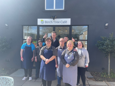 Tom outside of Birch Tree Cafe with a group of their staff. They are smiling and holding their thumbs up.