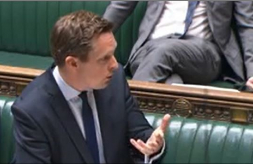 Tom stood in the House of Commons, answering a question. He gestures away from himself while doing so. 