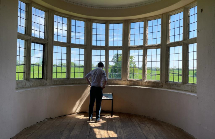 Tom standing in a large bay window at Kirby Hall, reading an information board