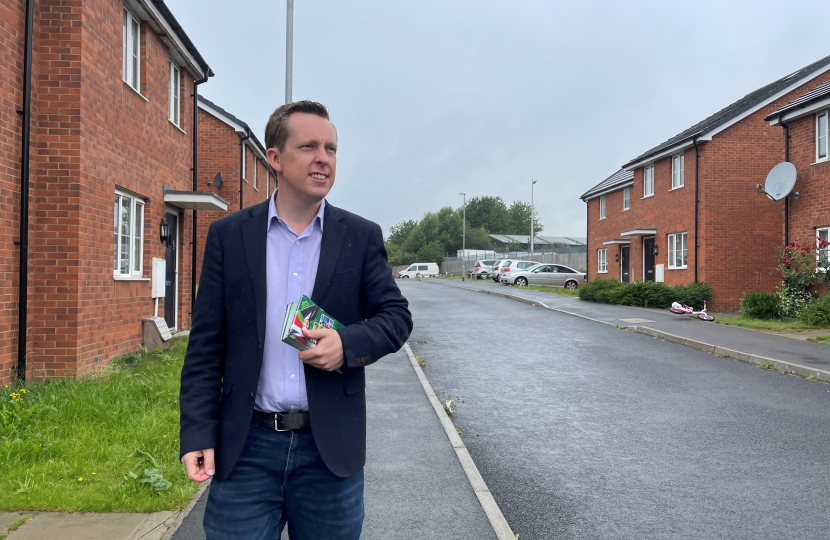 Tom stood on a street in Corby Old Village holding his MP contact cards.