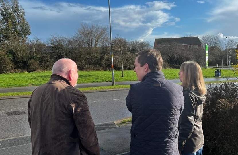 Tom, stood with his back to the camera, alongside two local residents with whom he is having a conversation. The previously proposed mast location is in the background of the photo, which is a green space next to the road.