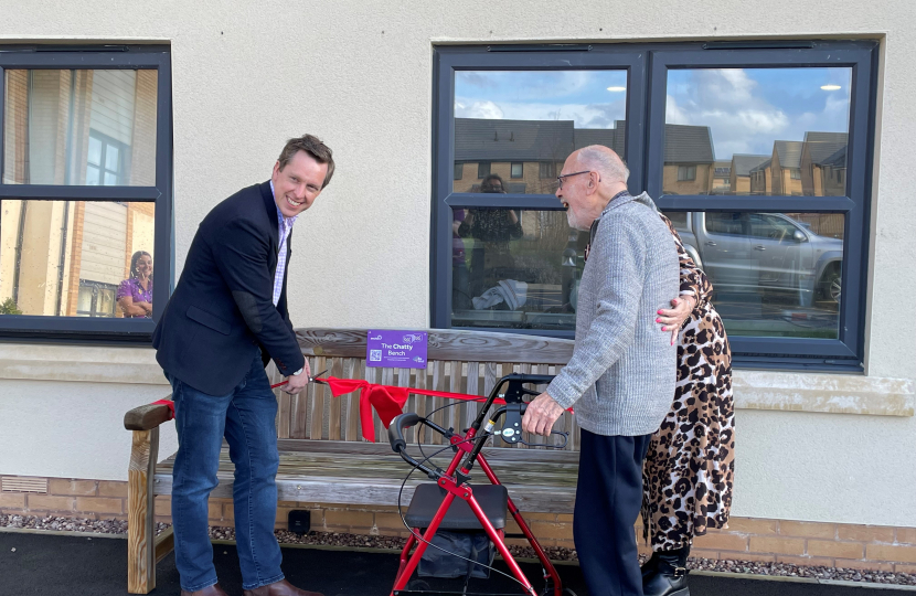 Tom Pursglove MP, with Harry, a resident at Priors Hall Care Home, unveiling the new Chatty Bench and cutting a red ribbon.
