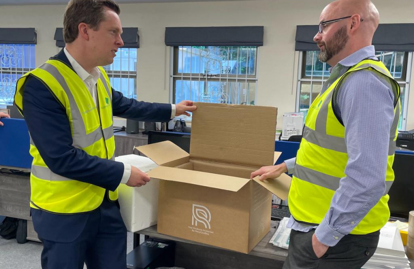 Tom stood talking to an employee of Goggleboxes. They are both wearing hi-viz jackets and are looking at one of the cardboard boxes designed and produced by the business