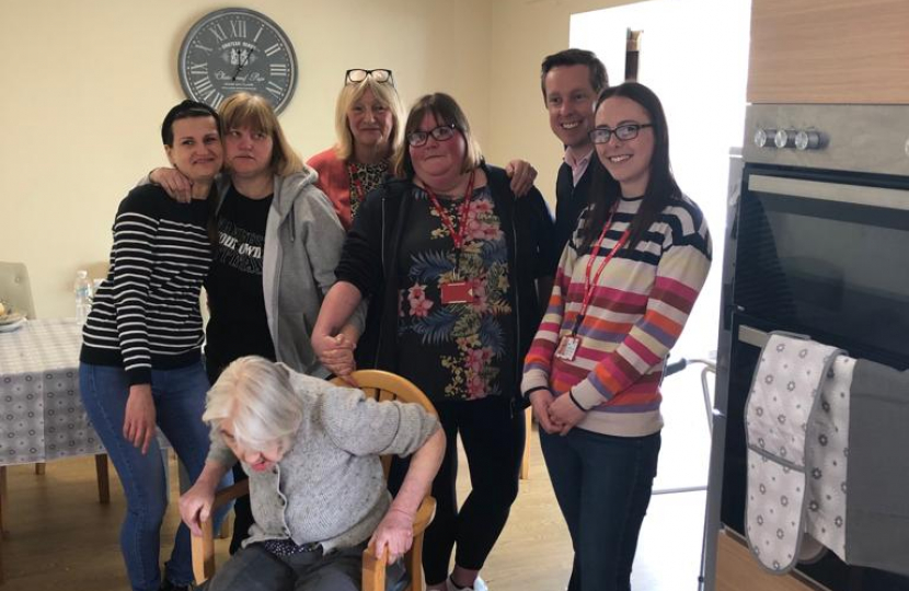 Tom smiling alongside six residents and carers at Mencap in Corby