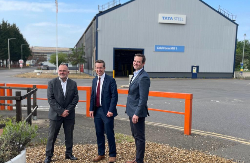 Tom stood smiling next to two employees of Tata Steel, Corby. They are stood in front of one of Tata's buildings in Corby and the sky is blue
