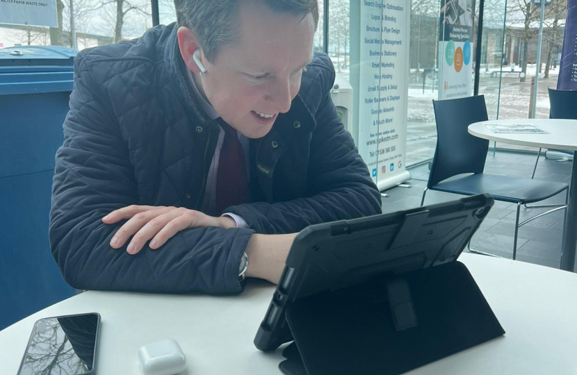 Tom in a virtual meeting with a representative from Vodafone. He is sat down, looking down at his tablet, smiling.