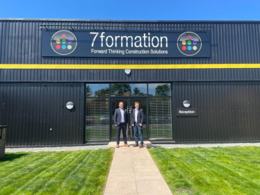 Tom and a representative from 7formation stand in front of the recently completed new company building, facing the camera with strong sunlight shining.