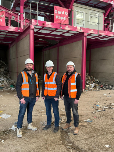 Tom Pursglove MP visit to Bailey's Skip Hire & Recycling. Tom is standing with two of their representatives; all are wearing hi-vis clothing and PPE. Waste sorting facilities are behind them.