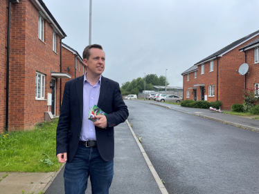 Tom stood on a street in Corby Old Village holding his MP contact cards.