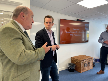 Tom in conversation with the Director of MPB. There is a screen in the background which reads 'Welcome! Induction and Enrolment for NVQ Programme'.