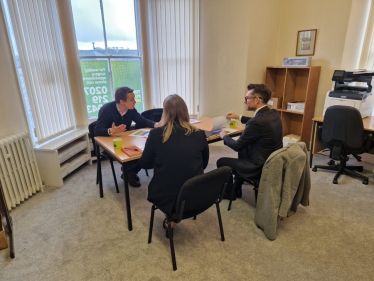 Tom in discussion with two representatives from Newlands Developments. They are all sat at a table. Tom is talking and gesturing with open hands.