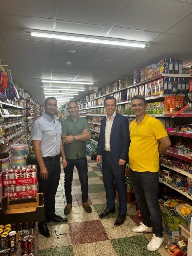 Tom stood with local shop owners in Euromarket. There are shelves full of products in the background