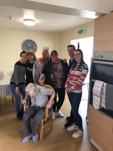 Tom smiling alongside six residents and carers at Mencap in Corby